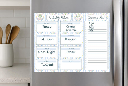 May include: A magnetic weekly menu and grocery list, featuring a floral and striped design in blue and white. The menu includes meal options like tacos, burgers, and steak. The grocery list section has a list of common items.