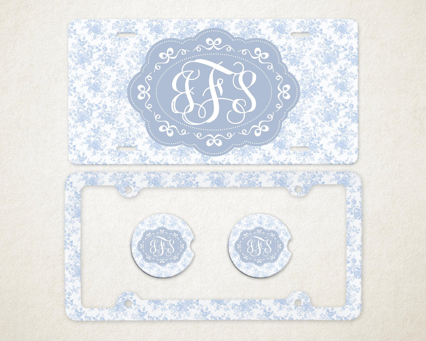 May include: A light blue license plate and frame set with a floral pattern. The license plate features a light blue oval with white initials. Two matching car coasters are also included.