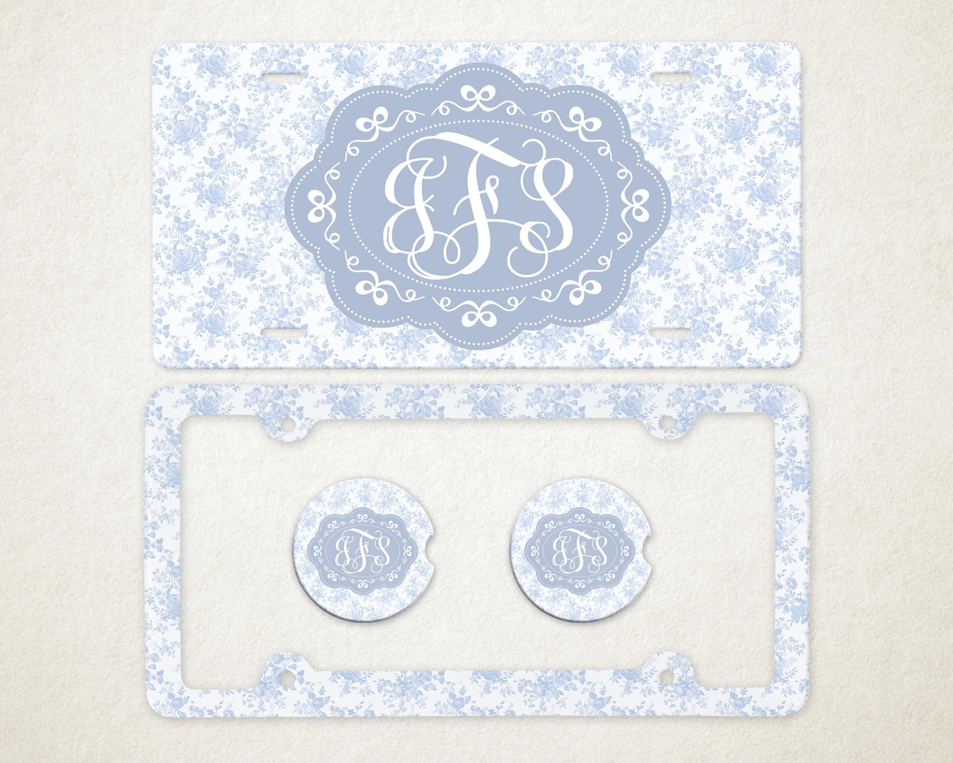 May include: A light blue license plate and frame set with a floral pattern. The license plate features a light blue oval with white initials. Two matching car coasters are also included.