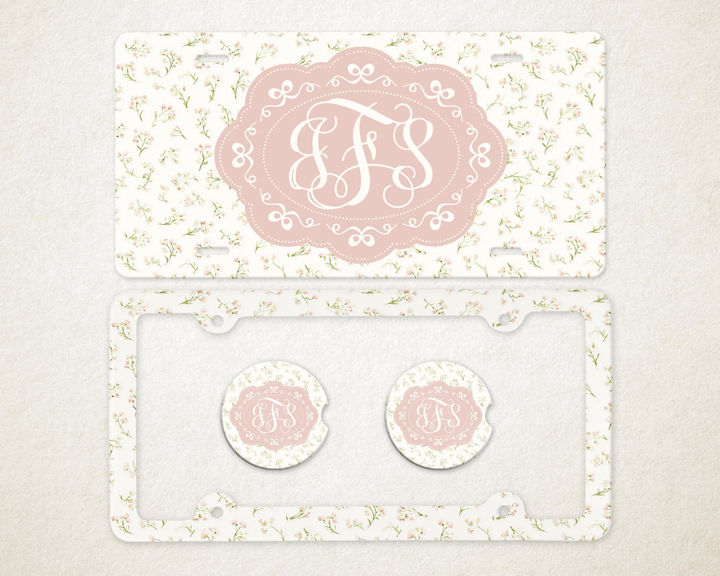 May include: A license plate, license plate frame, and two car coasters with a floral pattern. The license plate and coasters have a pink oval with the letters "JFS" in a white script. The license plate frame is clear.