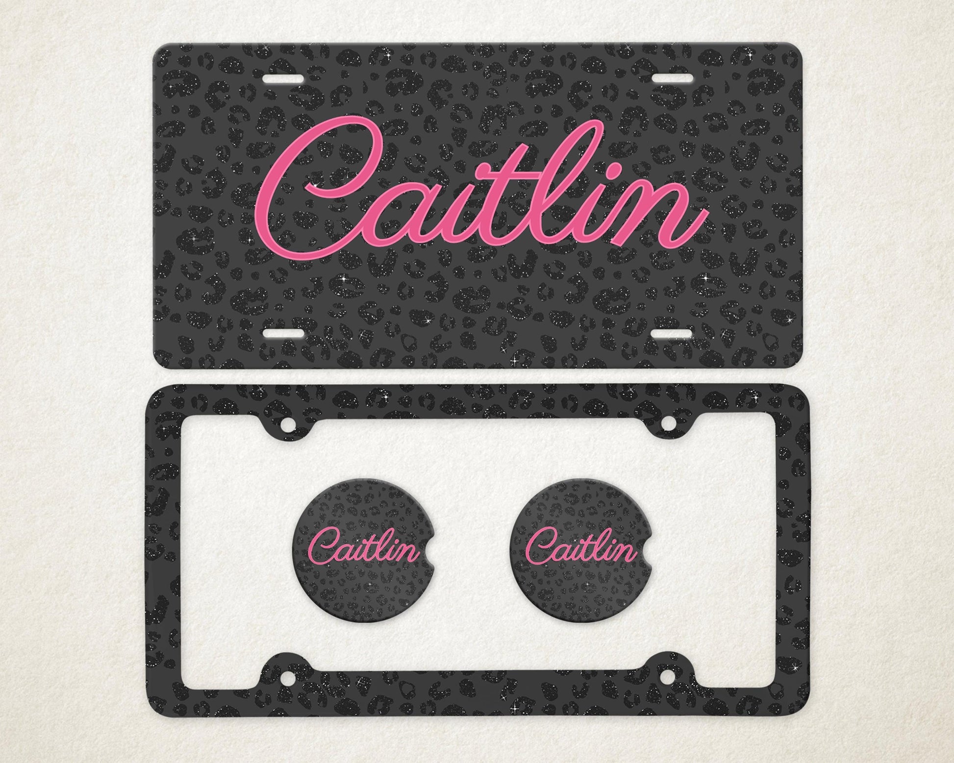 May include: A license plate and car coasters set. The license plate and coasters have a black leopard print design with the name "Caitlin" in pink script. The license plate frame is black.