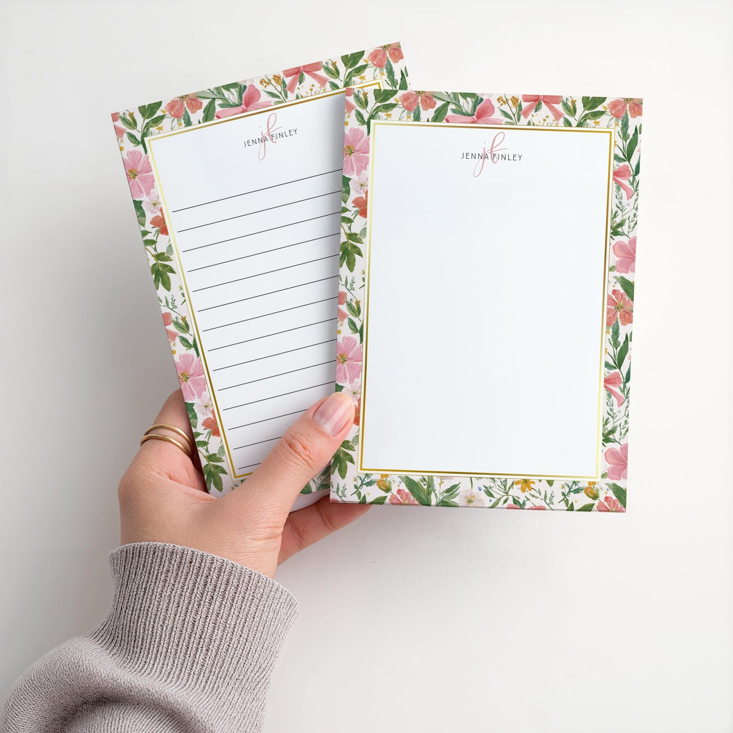May include: Two floral notepads with a gold border and the name "Jenna Finley" printed at the top. One notepad has lined paper, and the other is blank. The floral design features pink flowers and green leaves.